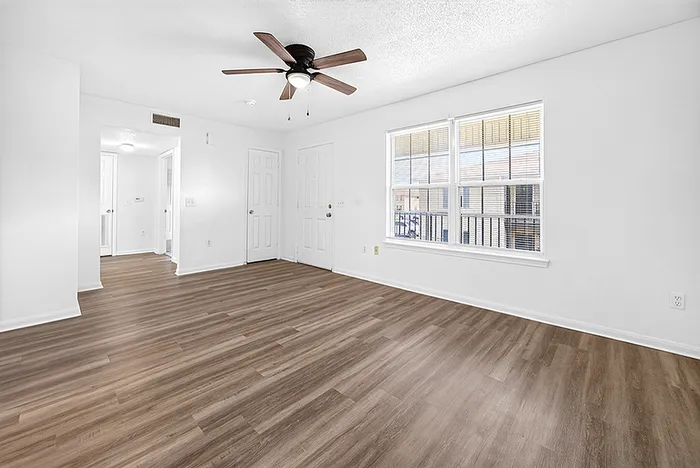 Bright and airy living space with sleek wood flooring, large window for natural light, and a stylish ceiling fan.
