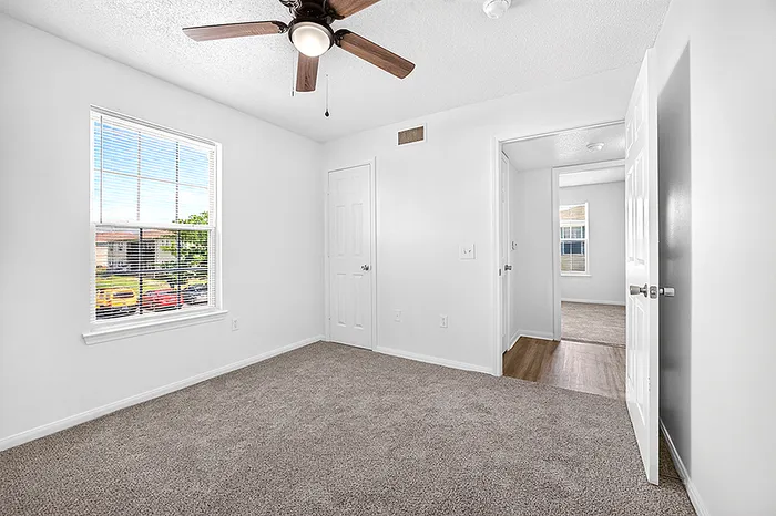 Bright and airy bedroom with plush carpeting, large window, and modern ceiling fan in a stylish apartment.