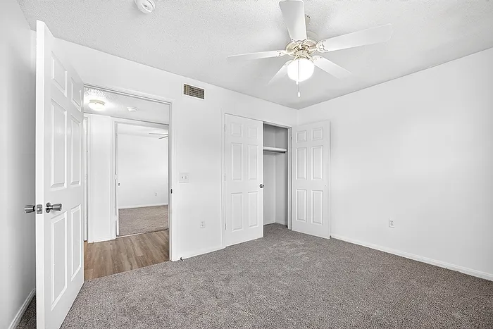 Bright bedroom with plush carpet, built-in closet, and ceiling fan, providing a comfortable and welcoming space.