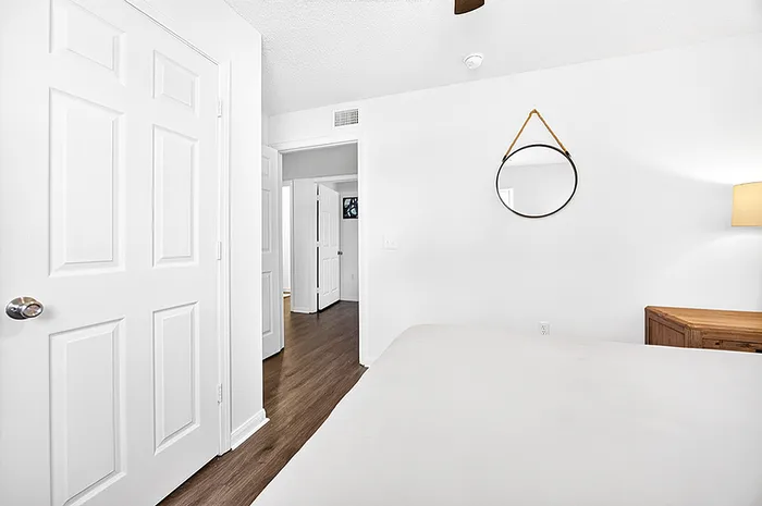 Bright, modern bedroom featuring sleek hardwood floors, a chic round mirror, and elegant white doors leading to an adjacent room.