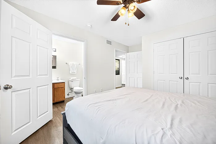 Bright bedroom with modern ceiling fan, attached bathroom, and ample closet space, perfect for comfortable living.
