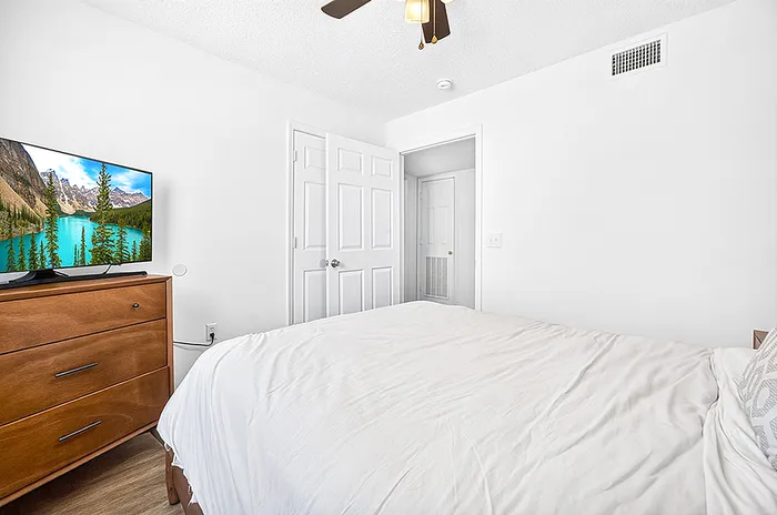 Bright and inviting bedroom with a cozy bed, sleek wooden dresser, and a flat-screen TV displaying a scenic landscape.