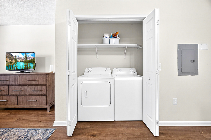 Modern apartment with built-in washing machine and dryer in a sleek laundry closet, complemented by a stylish cabinet and wall-mounted TV.
