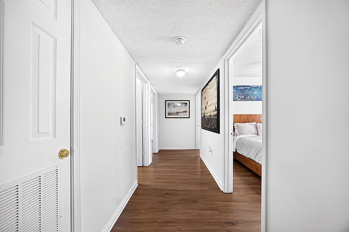 Bright and inviting hallway with modern wood flooring, leading to a cozy bedroom and featuring stylish wall art.