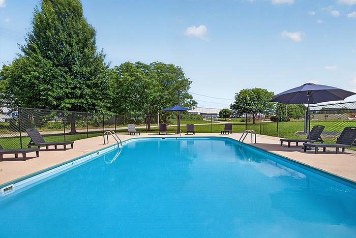 Inviting outdoor pool area with lounge chairs and umbrellas, surrounded by lush greenery and open sky.