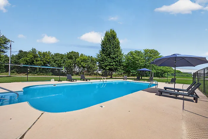 Inviting outdoor pool area with sun loungers and umbrellas, surrounded by lush greenery and clear sky.