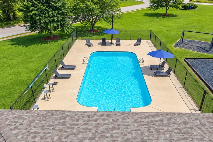 Inviting outdoor pool area with sun loungers and umbrellas, surrounded by lush green lawns, perfect for relaxation and recreation.