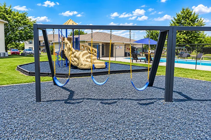 Charming outdoor playground featuring swings, a climbing structure, and a nearby pool under a sunny sky, perfect for family-friendly living.