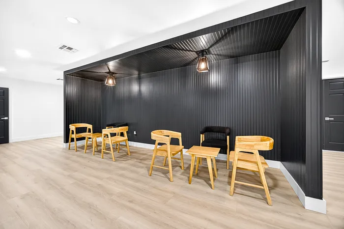 Modern communal area with sleek black walls, cozy wooden chairs, and warm ambient lighting, perfect for relaxation and socializing.