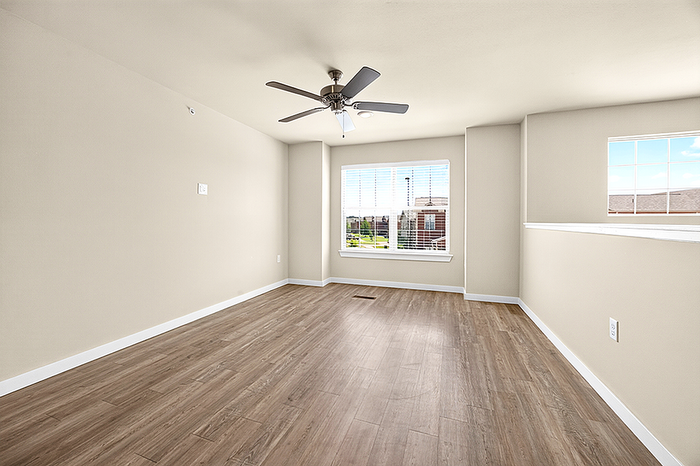 Bright and airy room with elegant wood flooring, large sunlit window, and modern ceiling fan offering a serene living space.