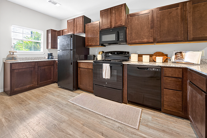 Modern kitchen with sleek dark wood cabinets, black appliances, and elegant light wood flooring.