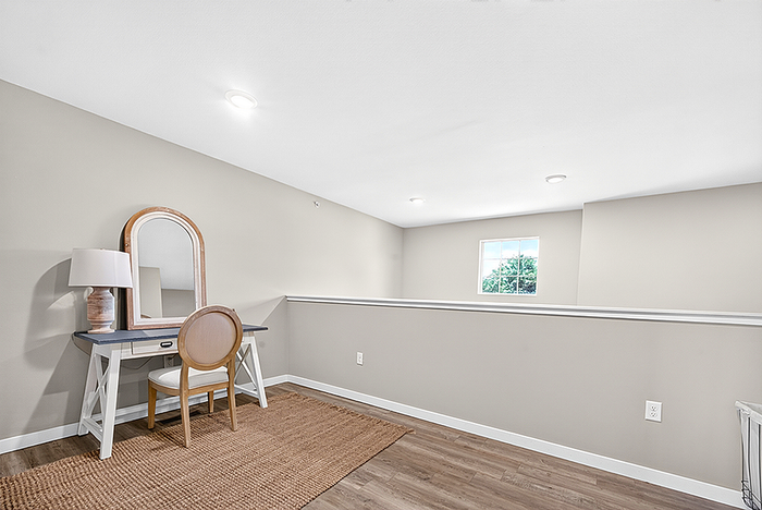 Bright and airy living space featuring a sleek writing desk with a stylish chair, under a modern lamp, on elegant hardwood flooring.