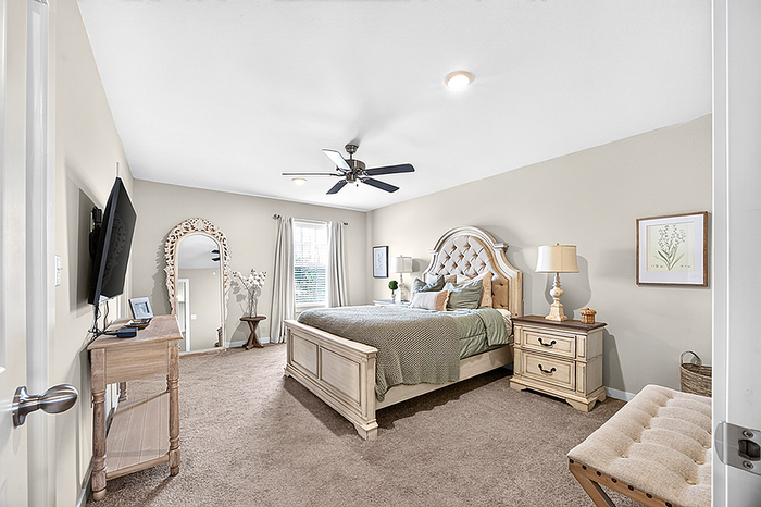Elegant bedroom with plush carpeting, stylish furniture, a large mirror, and a ceiling fan for comfort.