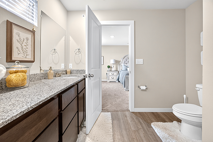Elegant bathroom with granite countertop and decorative accents leading to a cozy bedroom, featuring modern cabinetry and warm lighting.