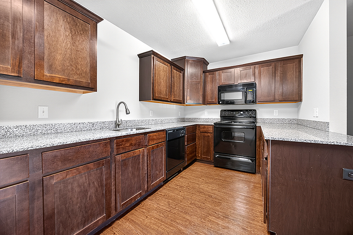 Modern kitchen with sleek granite countertops, dark wood cabinets, and state-of-the-art black appliances.