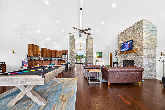 Luxurious open-concept living area with elegant stone fireplace, modern kitchen, plush leather furniture, and a pool table, offering a stylish and cozy atmosphere.