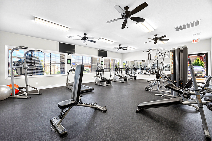 Bright and modern fitness center equipped with state-of-the-art exercise machines and ceiling fans for a refreshing workout experience.