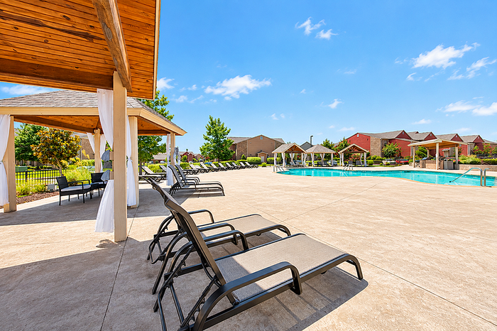Luxurious apartment complex featuring a sunlit pool area with sleek lounge chairs and shaded cabanas, perfect for relaxation.