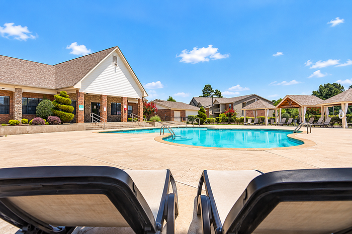Inviting resort-style pool area surrounded by charming brick architecture and lush landscaping under a bright blue sky.