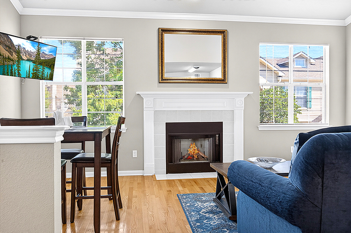 Bright and welcoming living room featuring a cozy fireplace, elegant wood floors, and large windows with scenic views.