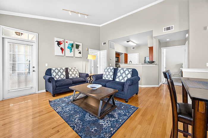 Bright and inviting living room featuring stylish blue sofas, elegant hardwood floors, and a cozy open-concept design leading to a modern kitchen.