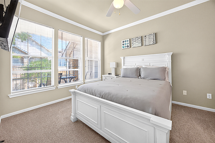 Bright and spacious bedroom with elegant white furniture, large windows offering abundant natural light, and modern wall art.