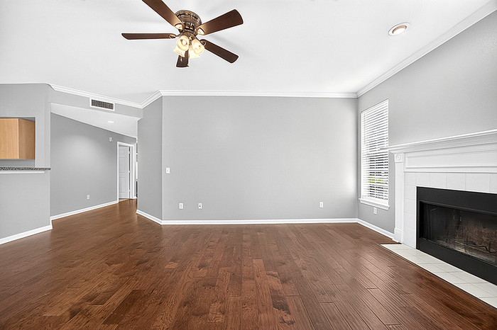 Chic open living space with sleek hardwood floors, cozy fireplace, and modern ceiling fan, bathed in natural light.