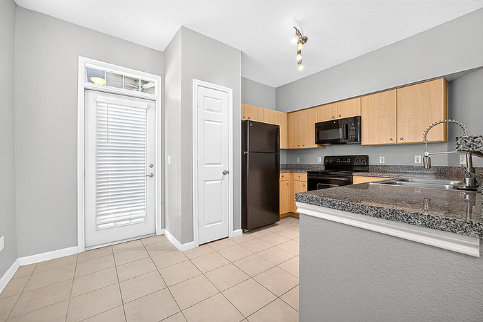 Modern kitchen with sleek granite countertops, black appliances, and light wood cabinetry, featuring elegant pendant lighting and a convenient door to outside.