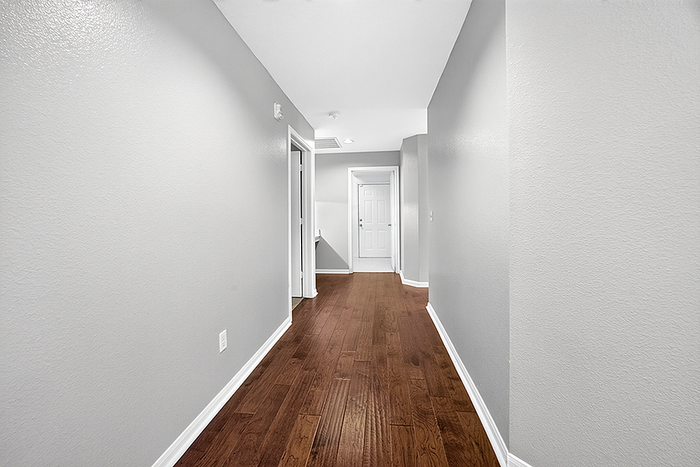 Inviting hallway with sleek hardwood floors and modern gray walls, leading to a bright interior space.