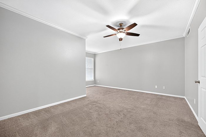 Spacious and airy room with plush carpeting, modern ceiling fan, and elegant neutral tones for a serene living space.