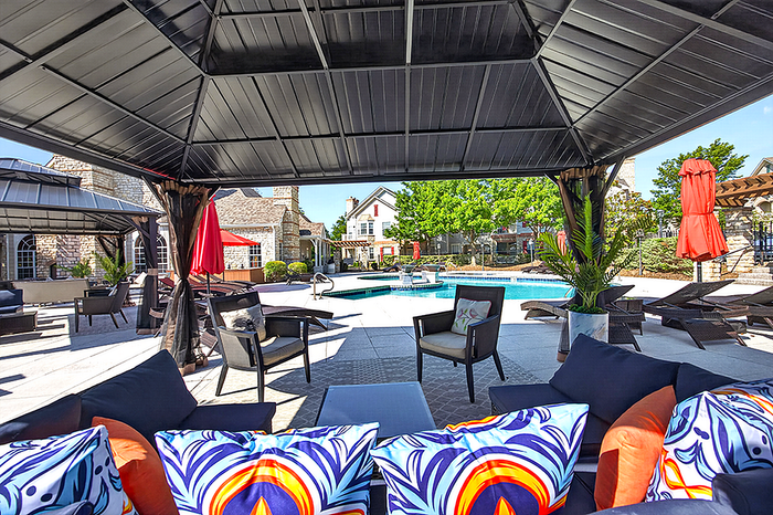 Luxurious outdoor lounge area with vibrant cushions, shaded seating, and a sparkling pool surrounded by lush greenery.