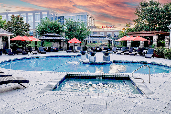 Luxurious apartment amenities with a sparkling pool, cozy sun loungers, and vibrant red umbrellas set against a stunning sunset backdrop.