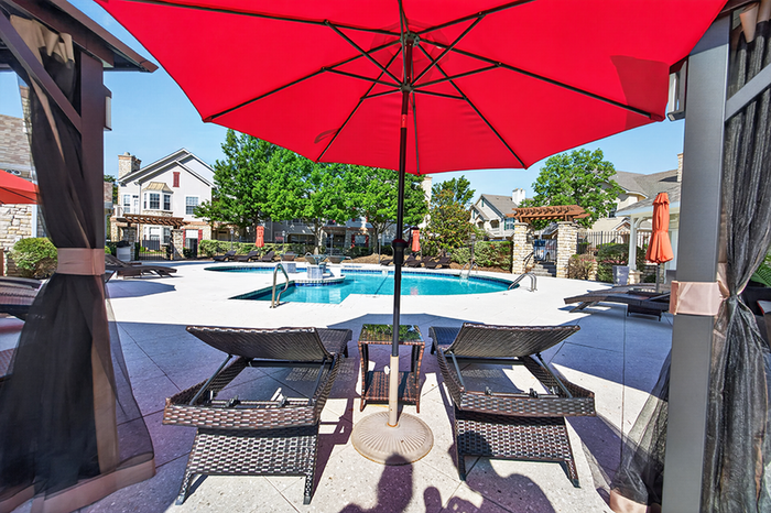 Charming poolside retreat with elegant loungers under vibrant red umbrellas, surrounded by lush greenery and cozy outdoor accents.