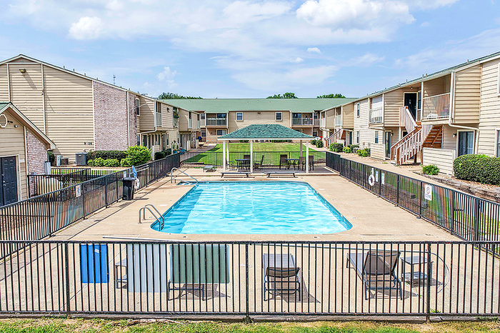 Inviting apartment complex showcasing a sunlit swimming pool, surrounded by well-maintained greenery and modern two-story buildings.