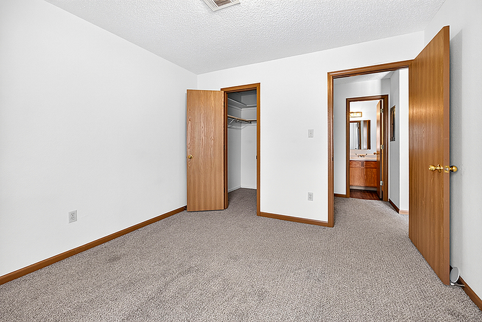 Inviting bedroom with plush carpeting, featuring dual wooden doors, including a convenient walk-in closet and access to a cozy bathroom.