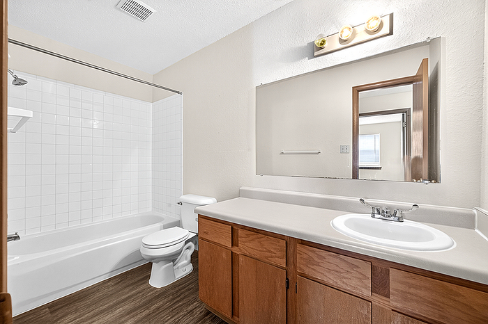 Bright and spacious bathroom featuring elegant wooden cabinetry, a large vanity mirror, and a classic bathtub with sleek tile surrounds.