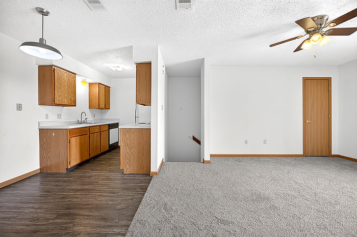 Bright open-plan space featuring a modern kitchen with wood cabinetry, a cozy living area, and elegant ceiling fan lighting.