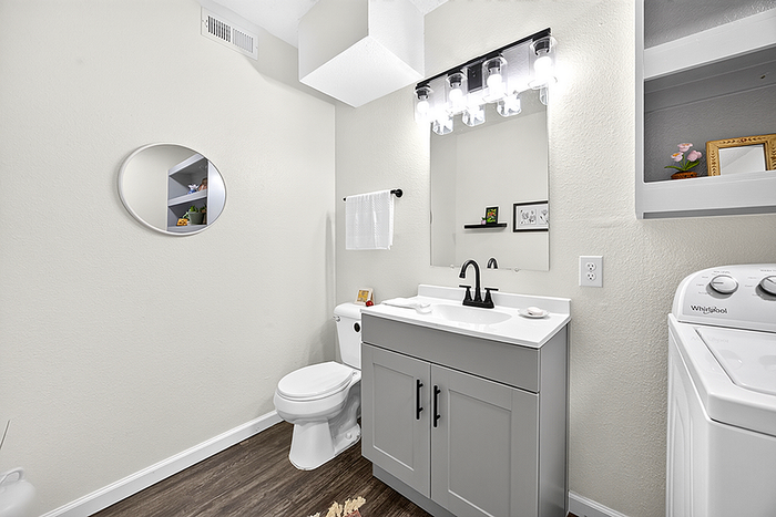 Modern bathroom with chic vanity, sleek round mirror, and in-unit laundry, illuminated by bright, stylish lighting.