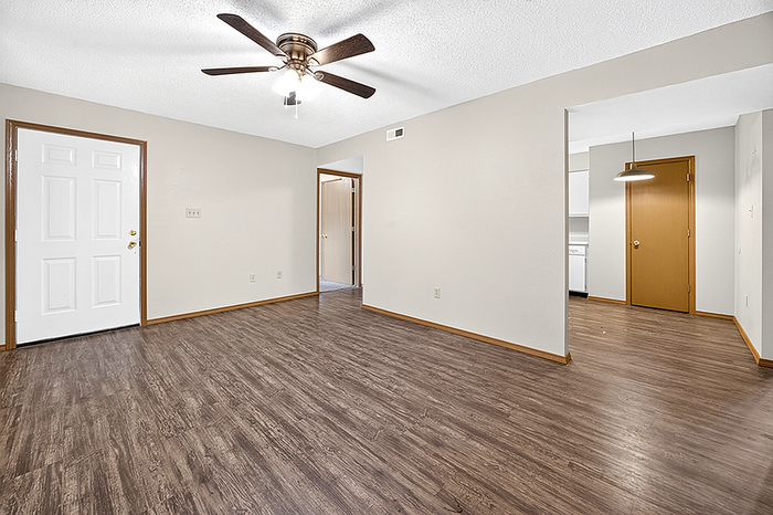 Spacious interior featuring elegant wood flooring, modern ceiling fan, and open layout leading to a cozy kitchen area.