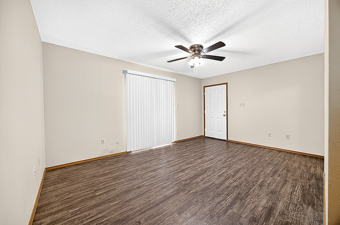 Bright and spacious living room with elegant wood flooring, ceiling fan, and sliding glass door; perfect for modern living.