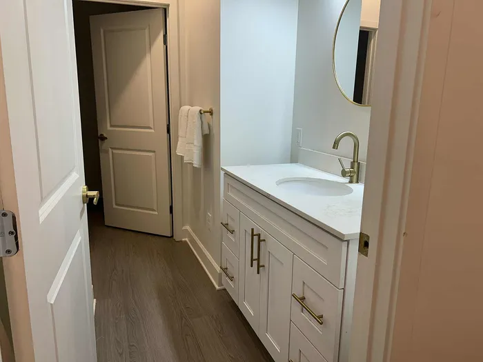 Elegant bathroom featuring a modern white vanity with gold fixtures, round mirror, and sleek hardwood flooring.