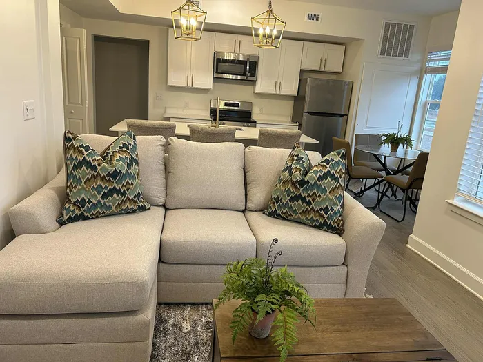 Inviting open-concept living space featuring a cozy beige sofa with patterned pillows, modern kitchen, and elegant dining area.