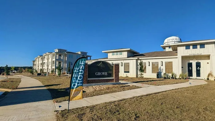 Charming modern apartment complex, 'Grove,' set against a bright blue sky with inviting open house signage, lush greenery, and spacious pathways.