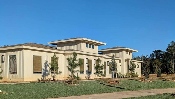 Charming modern bungalow with large windows and a neatly landscaped garden, basking in bright sunlight.