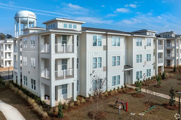 Elegant modern apartment building with spacious balconies, surrounded by greenery and a clear blue sky.