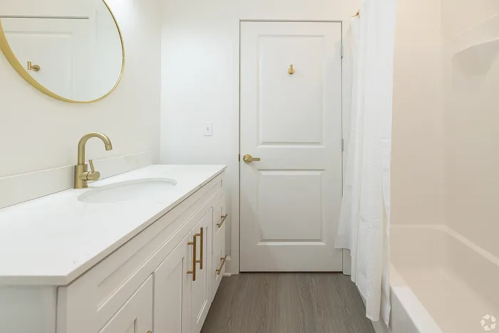 Elegant bathroom with a marble countertop, gold fixtures, and a round mirror adding luxury to a serene space.