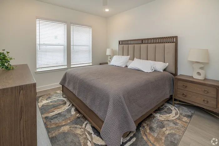 Inviting bedroom with sleek wooden furniture, cozy king-sized bed, and a modern aesthetic, bathed in natural light from large windows.