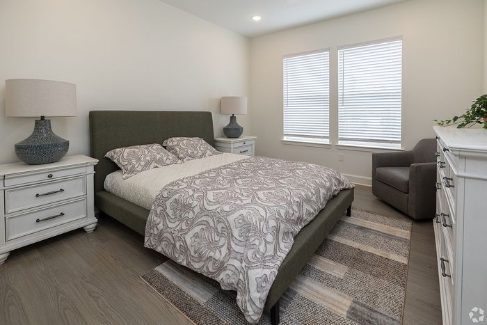Elegant bedroom with a stylish green upholstered bed, cozy neutral decor, and ample natural light from large windows.