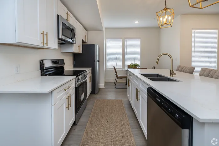 Modern kitchen with sleek white cabinetry, elegant gold fixtures, and a spacious island under chic pendant lights.