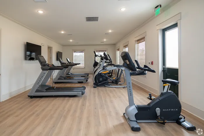 Modern apartment gym with state-of-the-art treadmills and elliptical machines, featuring sleek wooden flooring and natural light.